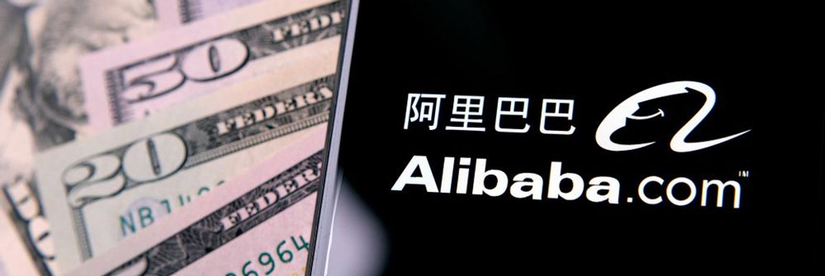 50, 20 és 5 dolláros bankjegyek egy telefon mögött, amin az Alibaba.com felirat látható kínai han írással kísérve