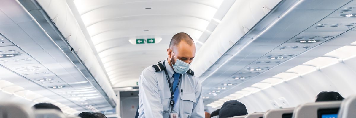 A Delta Air Lines légitársaság kék inges légi tisztje, munkavállalója kék maszkban járja a repülőt és gyűjti a szemetet egy fekete szemeteszsákba
