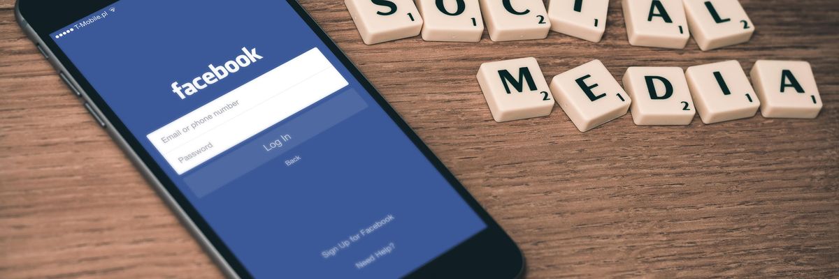 A Facebook alkalmazás kezdőoldala egy okostelefon képernyőjén, mellette social media felirat betűkből kirakva