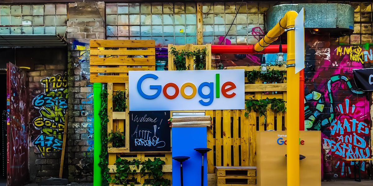 A Google logója egy sárga raklapokból összeállított installáción egy összegraffitizett fal előtt