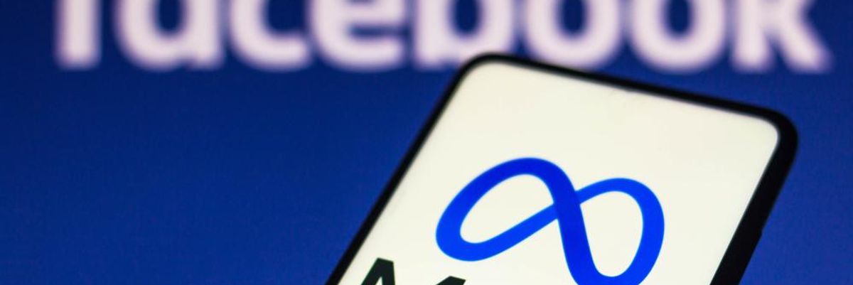 A Meta logója egy okostelefonon, ami egy ember kezében van, a háttérben a Facebook felirata látható egy kék felületen