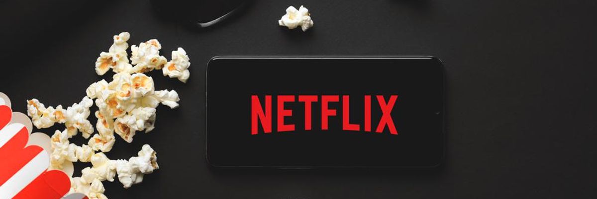 A Netflix logója egy okostelefon képernyőjén, körülötte popcorn, egy napszemüveg, egy fülhallgató, egy klaviatúra és egy kávéscsésze látható