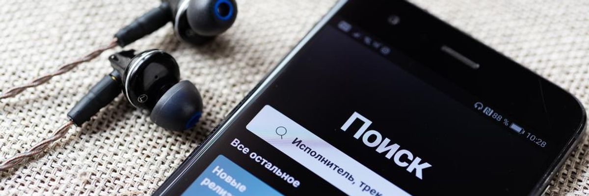 A Spotfy kezdőoldala orosz nyelven, a telefon mellett egy pár fülhallgató látható