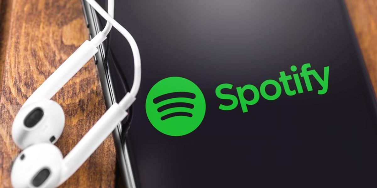 A Spotify logója egy okostelefonon, ami mellett egy pár fülhallgató található egy fa felületen