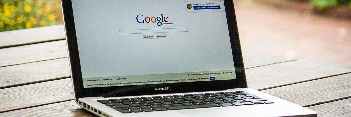 A szabadban egy faasztalon látható egy okostelefon és egy laptop, amelyen a Google kezdőlapja van behozva