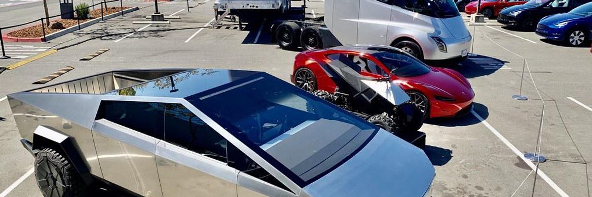 A Tesla ezüst színű kisteherautója, a Cybertruck egy parkolóban, egy Tesla quad, egy Tesla Roadster és egy elektromosnak tűnő kamion mellett