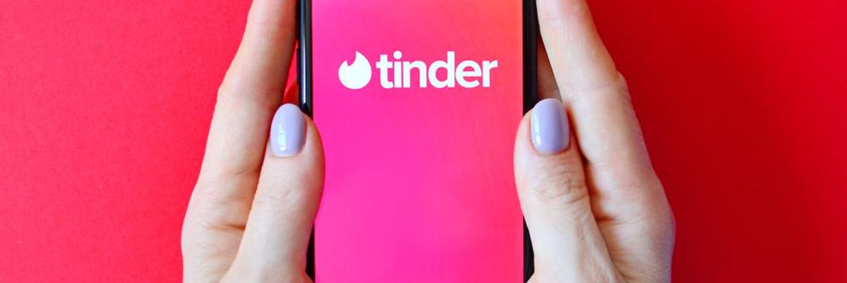 A Tinder tárkereső logója egy telefon képernyőjén, ami egy nő kezében van