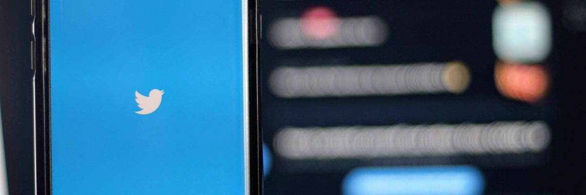 A Twitter logója (fehér madár kék alapon) látható egy okostelefon képernyőjén homályos háttér előtt