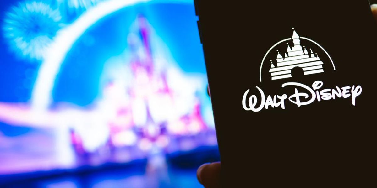 A Walt Disney logója egy okostelefon fekete képernyőjén, a háttérben a Walt Disney kastély sziluettje látható