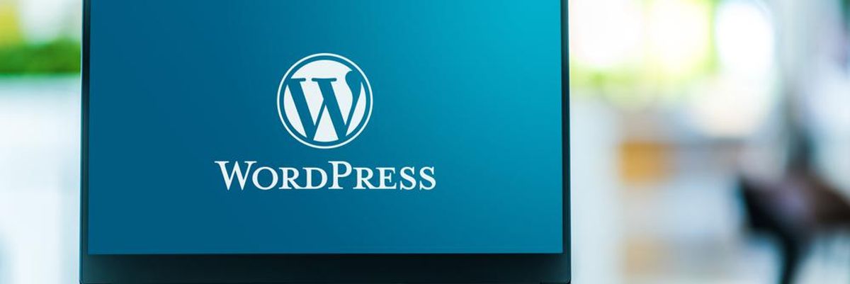 A WordPress kék-fehér logója egy laptop képernyőjén, ami egy asztalon van homályos háttérrel