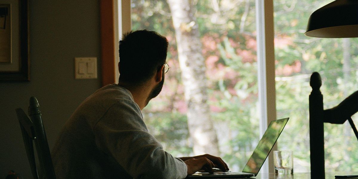 Ablakon kinéző otthon laptopján dolgozó férfi