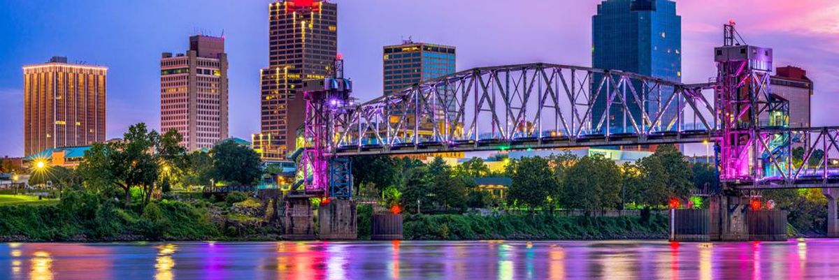 Arkansas állam fővárosa, Little Rock belvárosi látképe az Arkansas folyó mentén, napnyugtakor. Egy híd látható a folyó felett, a háttérben felhőkarcolók, bérházak tornyosulnak
