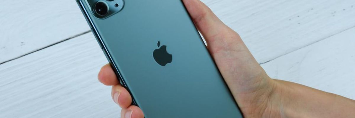 Az Apple egyik iPhoneját tartja kezében egy ember fehér fafelület felett, a márka új szolgáltatásra készül