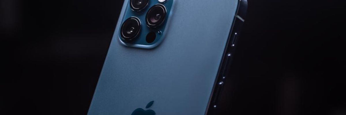 Az Apple egyik világoskék, három kamerás iPhone készüléke egy sötét szobában