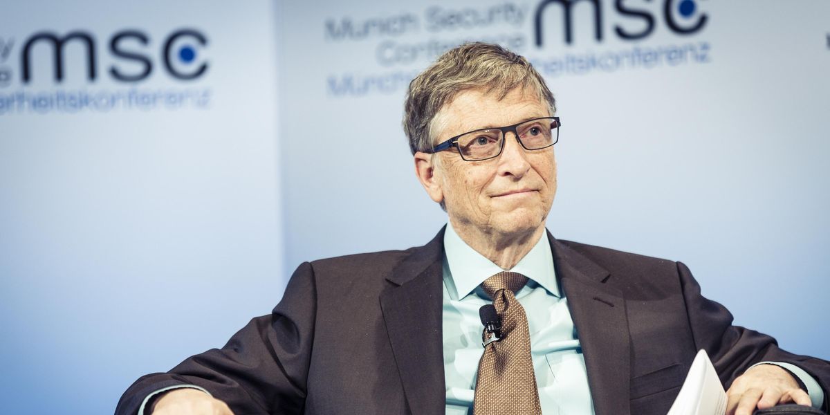 Bill Gates öltönyben ül egy székben és figyel