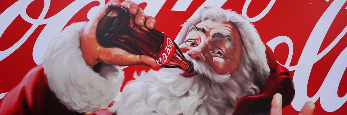 Coca-Cola Télapó Coca-Colát iszik egy Coca-Cola logó előtt