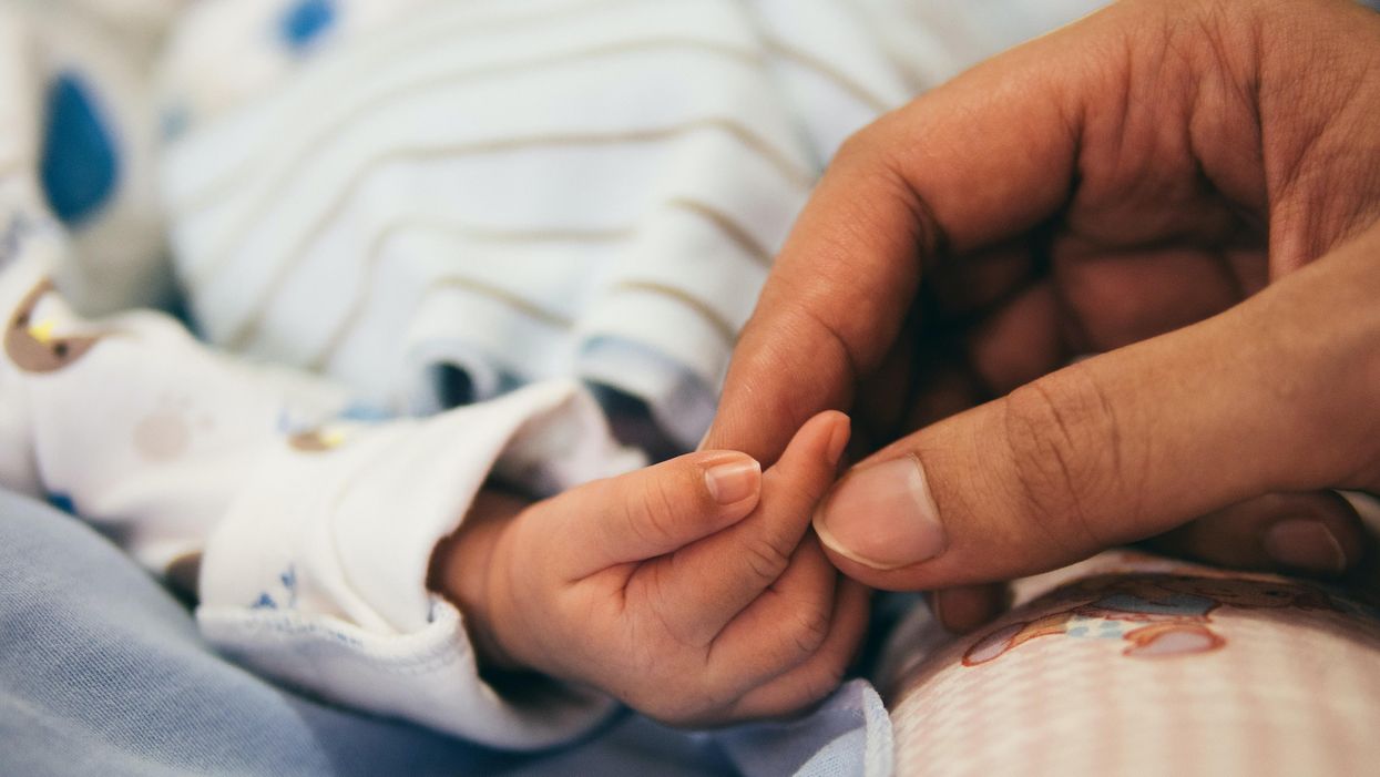 Egy csecsemő kezéhez ér hozzá a szülő keze.