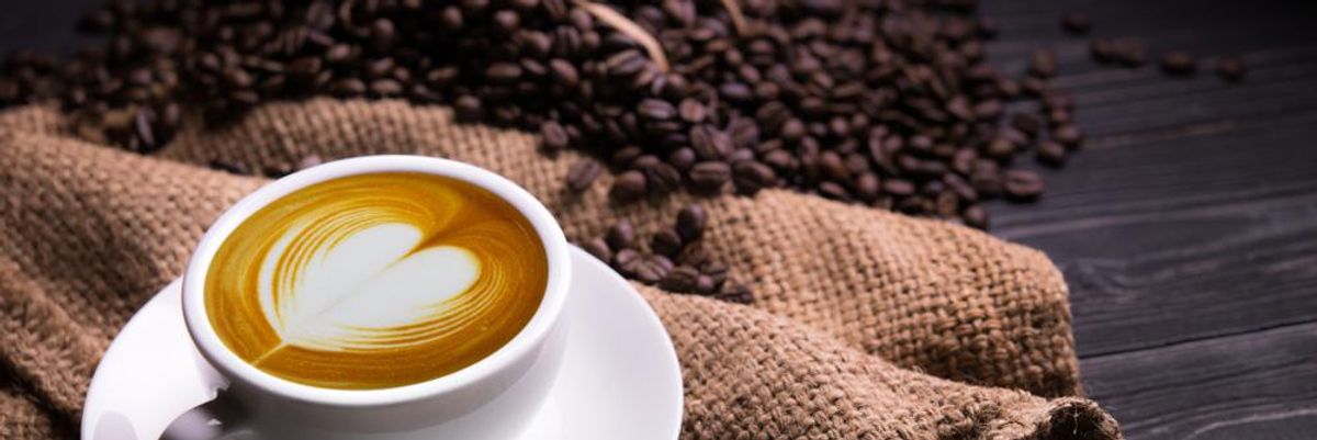 Egy csésze kávé szív alakú habbal egy zsákon, a háttérben kávébabok