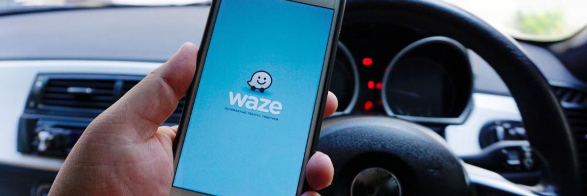 Egy ember a kezében tartja a telefonját, amin épp a Waze-t tölti be vezetés előtt a kocijában