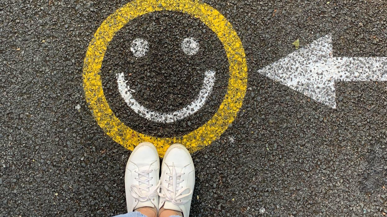 Egy ember áll egy mosolyt jelző, útra festett piktogram előtt.
