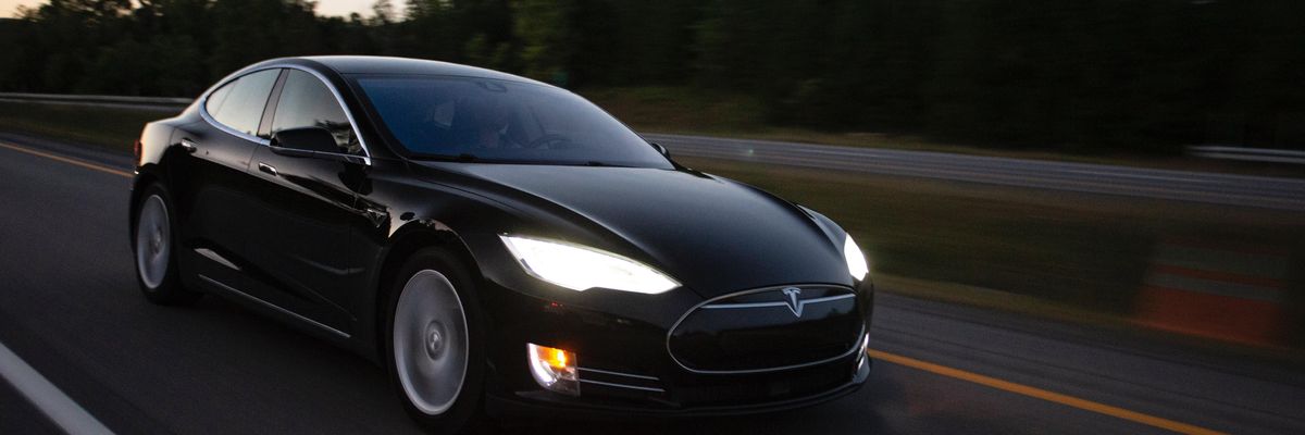 Egy fekete Tesla elektromos autó halad az autópályán a naplementében