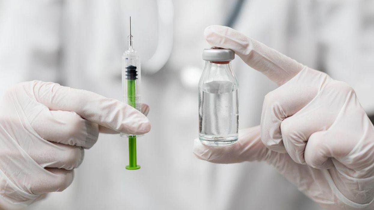 Egy injekcióstűt és az oltóanyagot tartalmazó üvegcsét tartja kezében egy egészségügyi dolgozó.