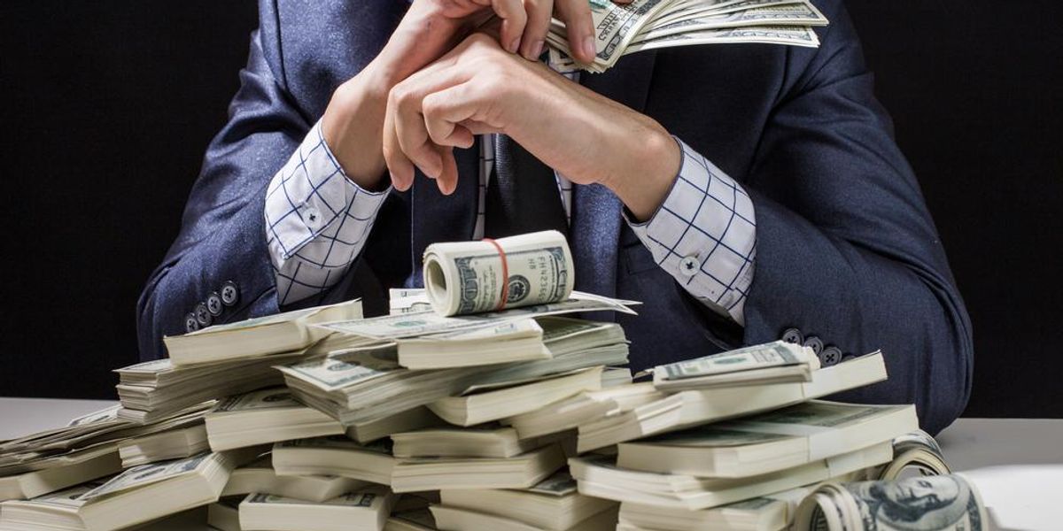 Egy kék öltönyös kripto-szakértő egy fehér asztalon könyököl, amin rengeteg pénz található
