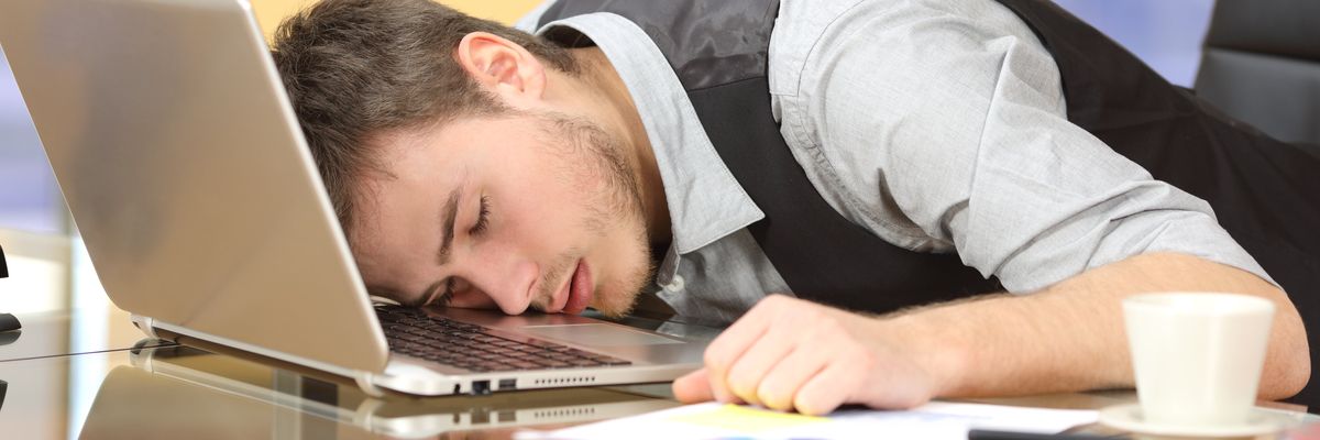 egy kimerült férfi fekszik a laptopján, elaludt munka közben