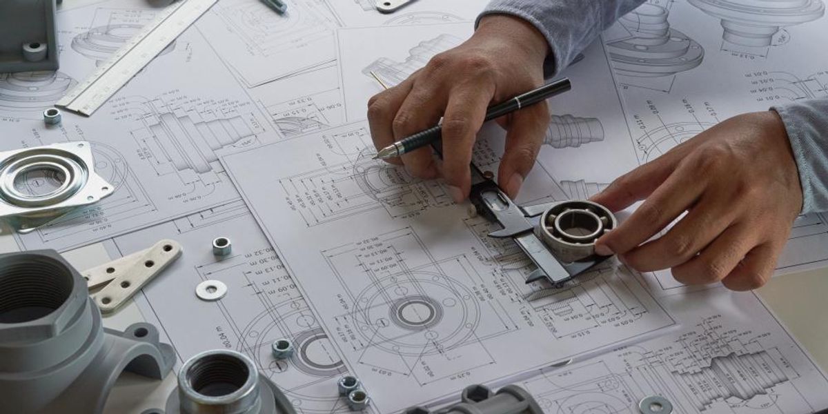 Egy mérnök a tervezőasztalán alkatrészeket tervez egy tolómérő és egy speciális ceruza segítségével