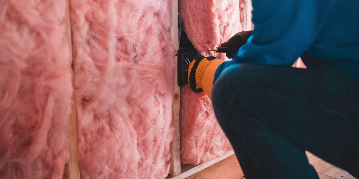 Egy munkás kivág egy darabot a rózsaszínű szigetelőanyagból a falon