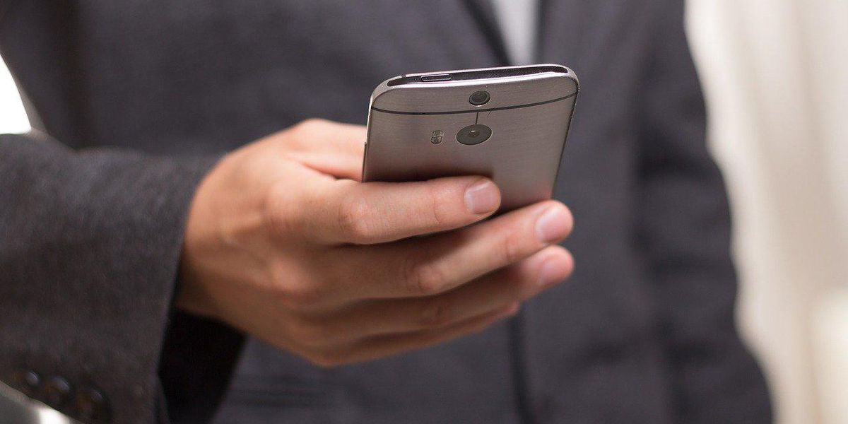 Egy öltönyös férfi a kezében tartja az okostelefonját, amin épp egy új nyelvet tanul a Duolingo segítségével