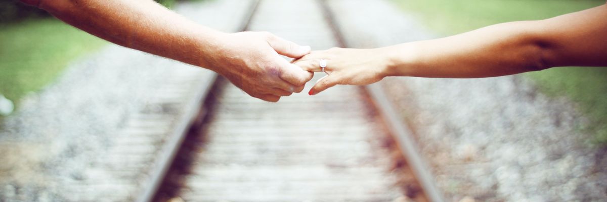 Egy pár egymásba fonódó keze a sínek felett