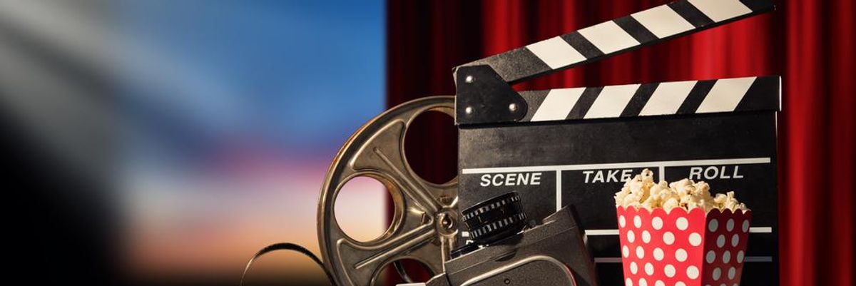 Egy retro kamera, egy csapó, egy filmszalag és egy adag popcorn van egy pódiumon vörös függöny és egy mozivászon előtt egy moziteremben