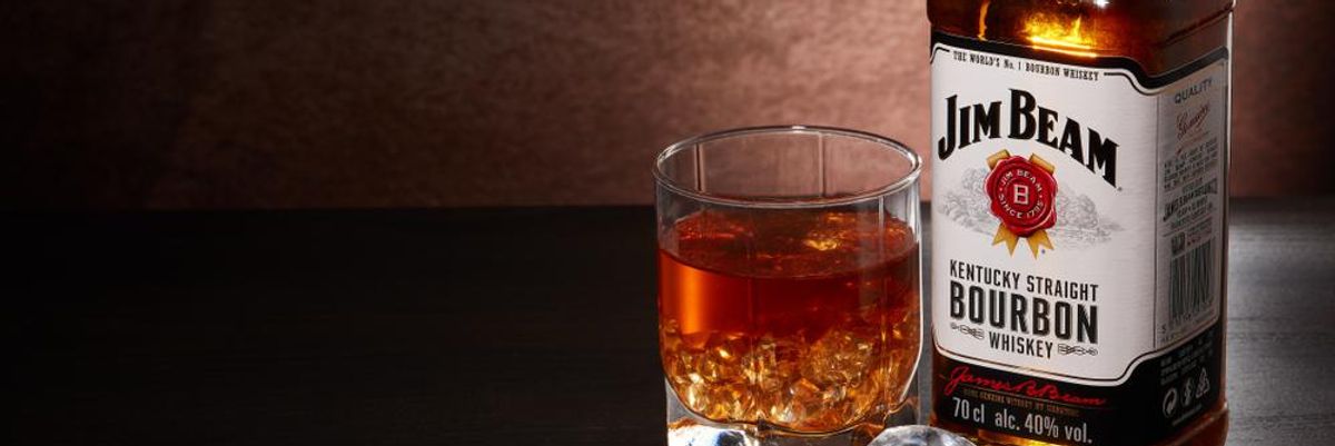 Egy üveg Jim Beam whiskey egy pohár whisky mellett, előttük jégkockák láthatók