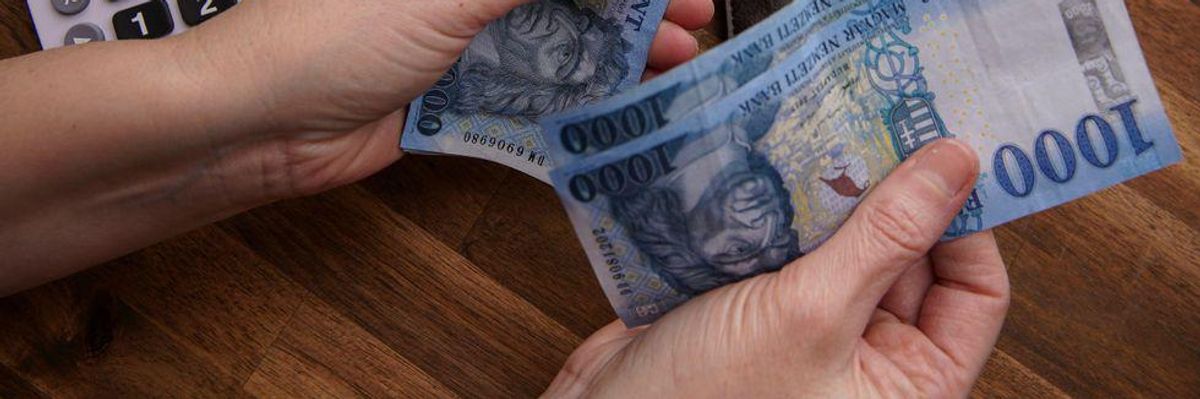 Ezer forintos bankjegyeket tart a kezében egy ember egy számológép mellett. 