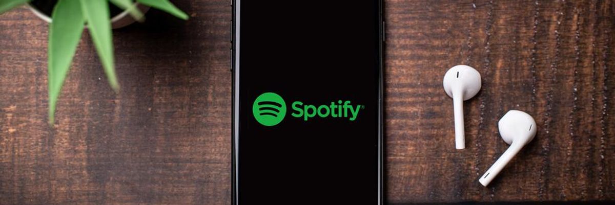 Faasztalra tett telefon és Apple Airpods, amelyekkel a Spotify hallgatására készül a tulajdonos egy növény mellett