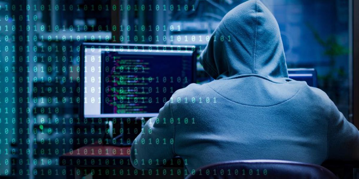 Fehér kapucnis pulcsi hacker ül egy számítógépnél, miután ingatlanportálokat fertőzött meg, a képen bináris számsorozat látható