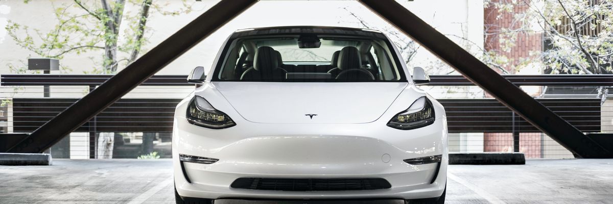 Fehér színű Tesla Model 3 áll egy parkolóház parkolójában nappal