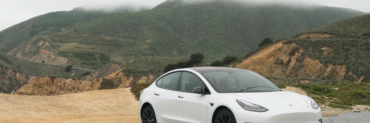 Fehér Tesla fekete alufelnikkel egy dombos vidéken, felhős időben