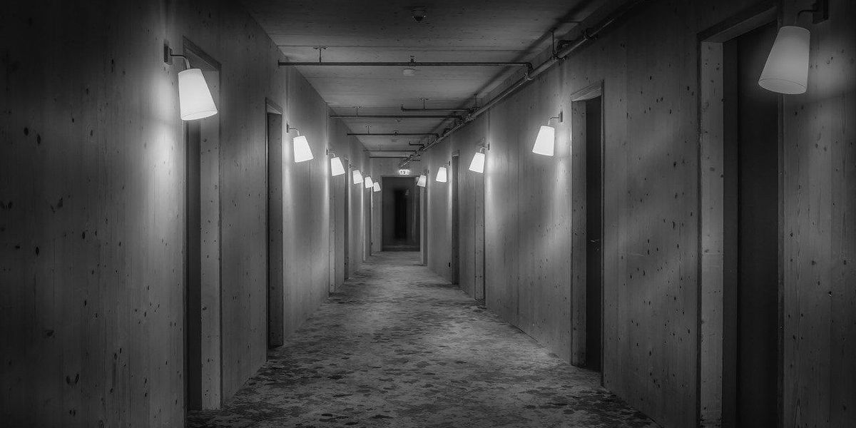Fekete-fehér kép egy szálloda üres folyosójáról, amit lámpák világítanak meg