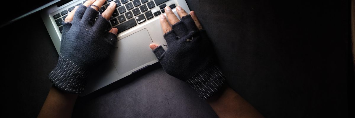 Fekete kesztyűs kezek dolgoznak egy laptop klaviatúráján