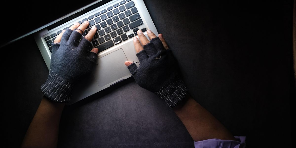 Fekete kesztyűs kezek dolgoznak egy laptop klaviatúráján