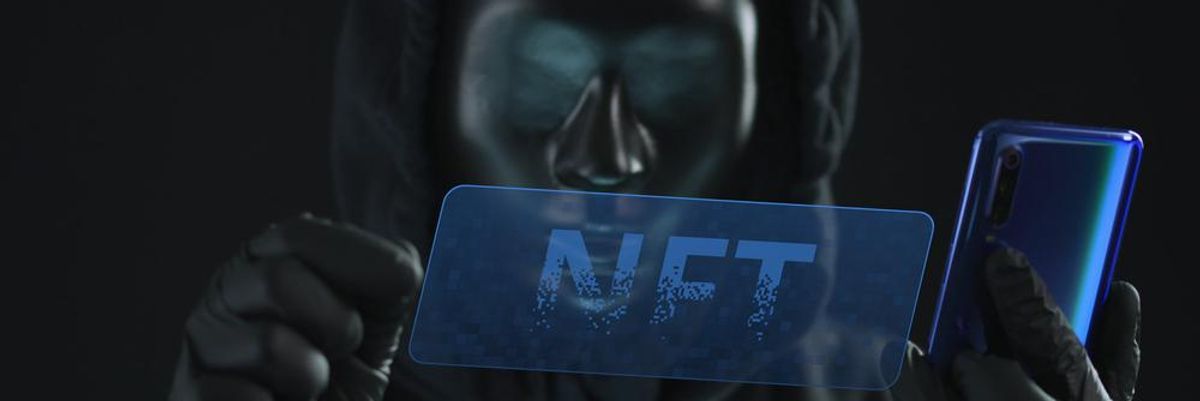 Fekete pulóveres, fekete kesztyűs, fekete maszkos ember egy NFT feliratú kék fóliát húzott le a kék okostelefonjáról