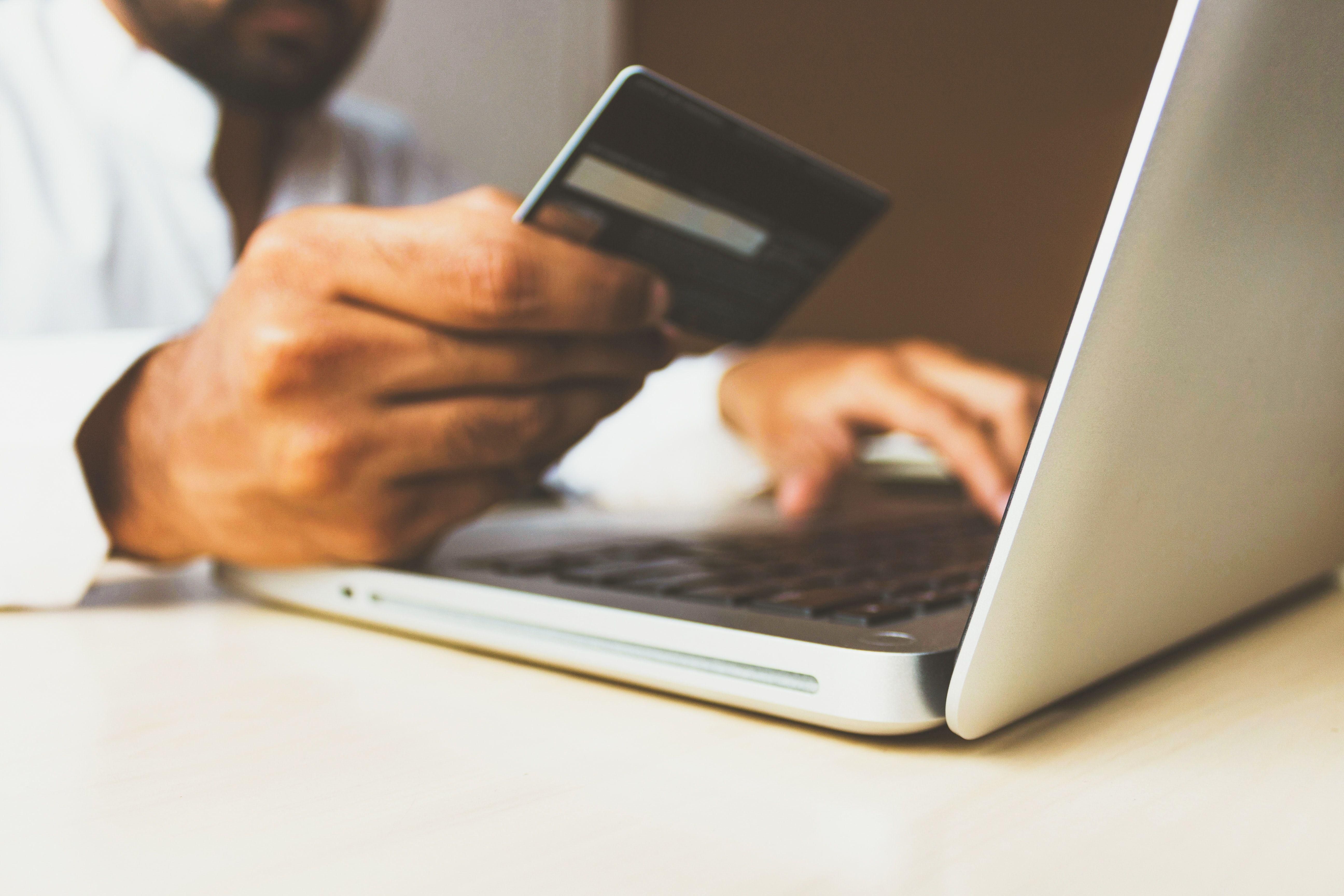 Bankkártyával, laptoppal online fizető ember keze