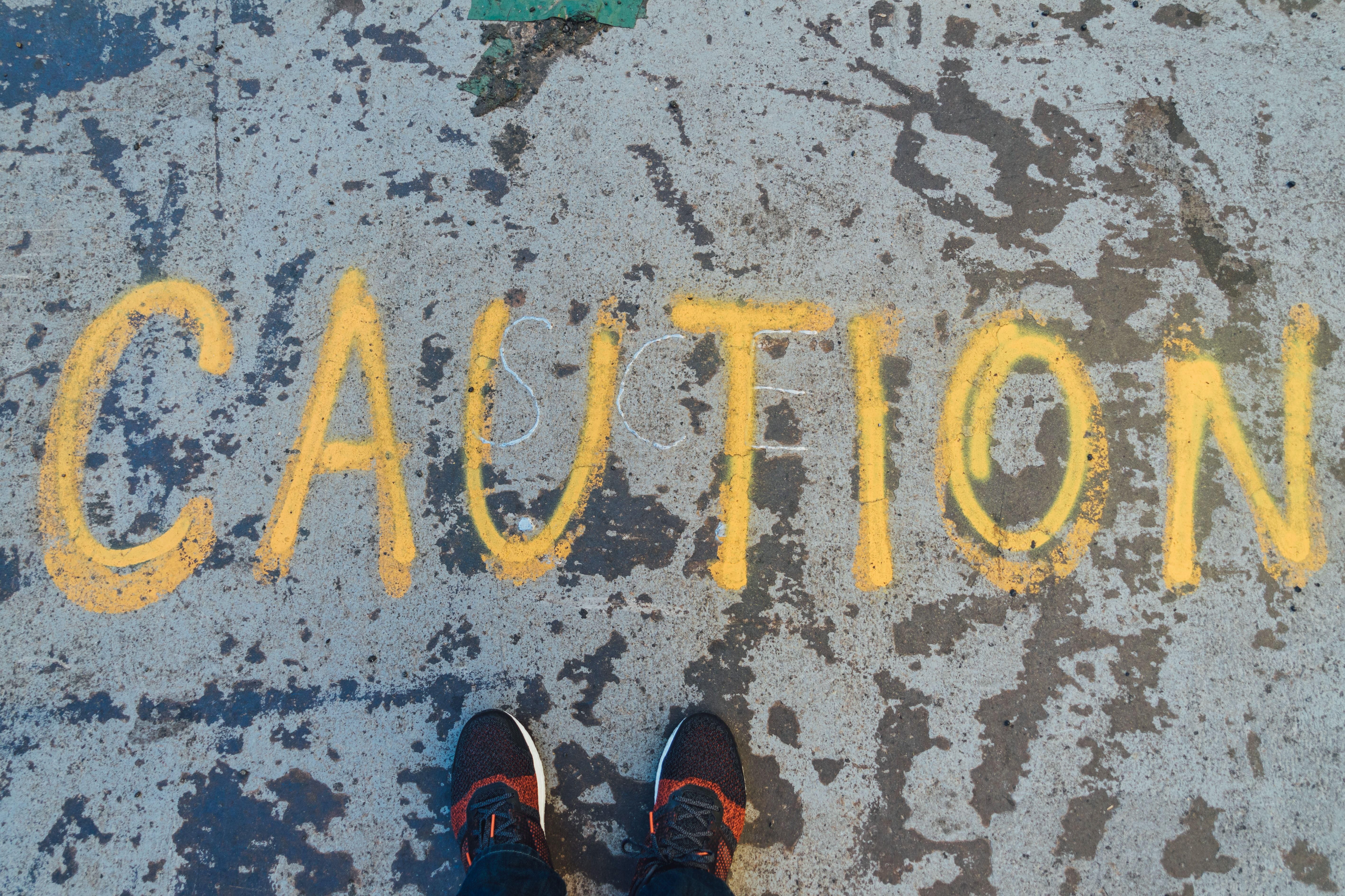 Járdára festett Caution felirat előtt álló ember lába