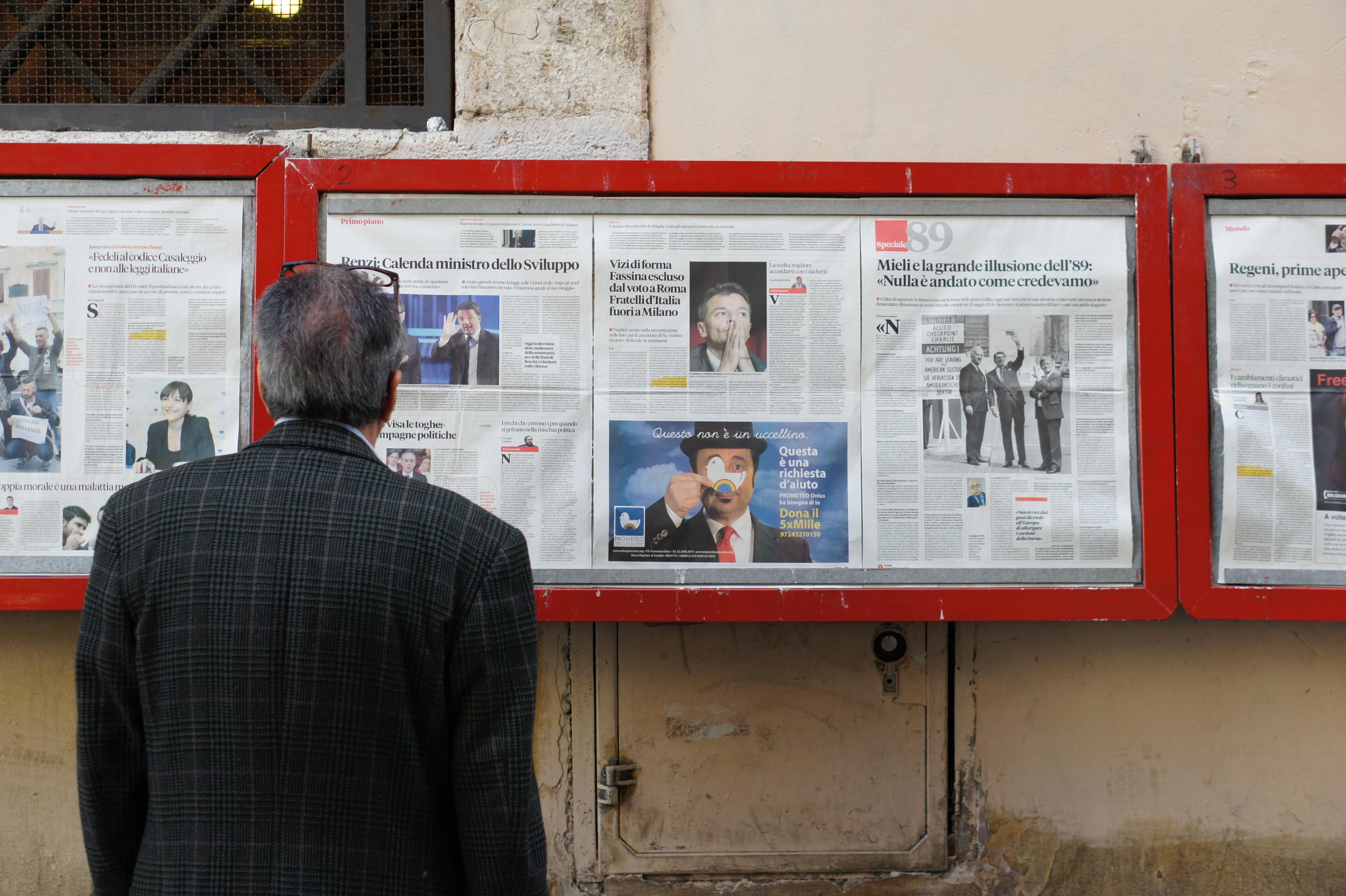 Egy öltönyös férfi olvassa a híreket különböző újságokból egyszerre