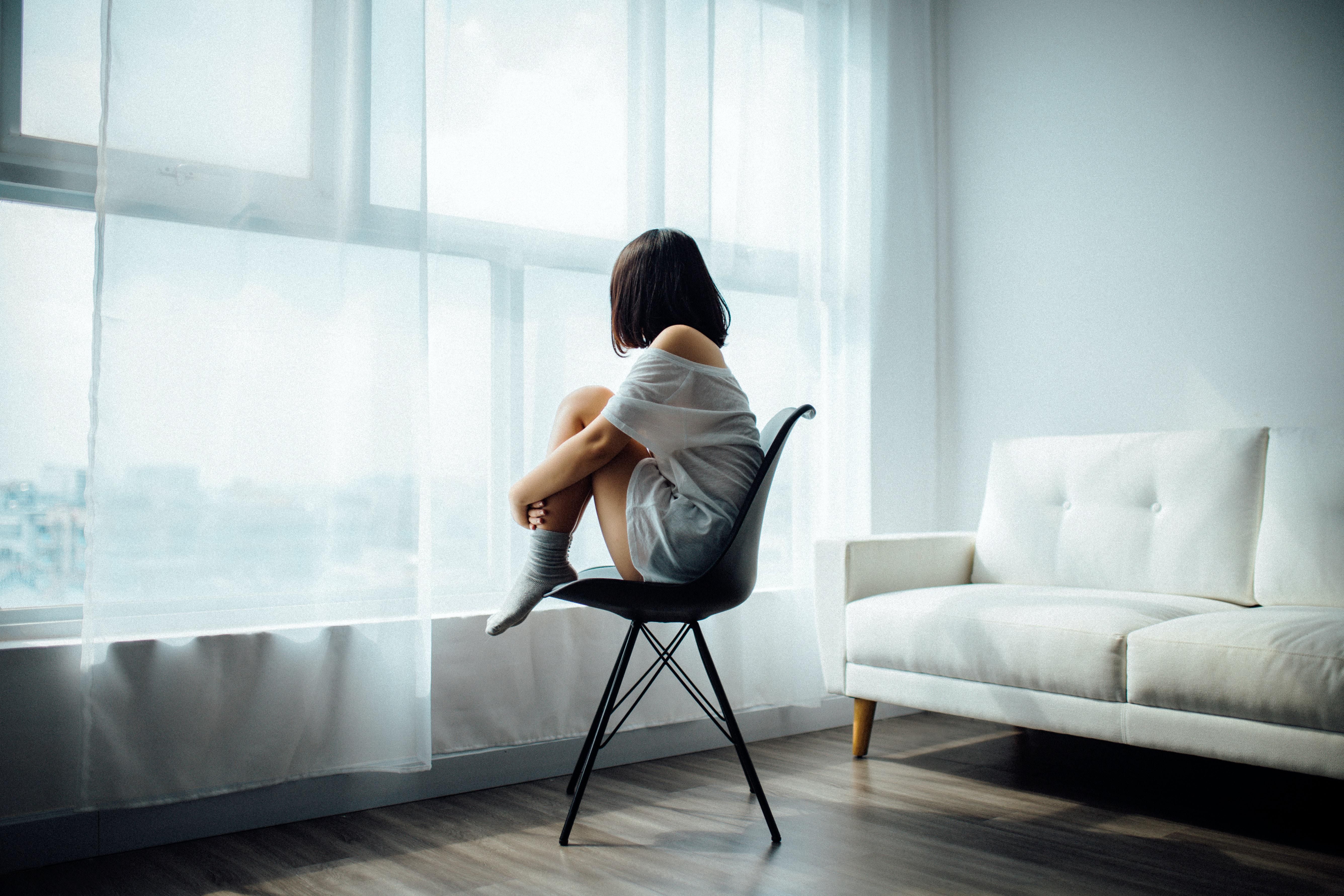 Rossz mentális egészségű TikTok felhasználó ül egy széken és néz kifele az ablakon
