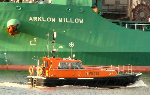 Révkalauz piros motorcsónakkal közelíti a zöld konténerhajót