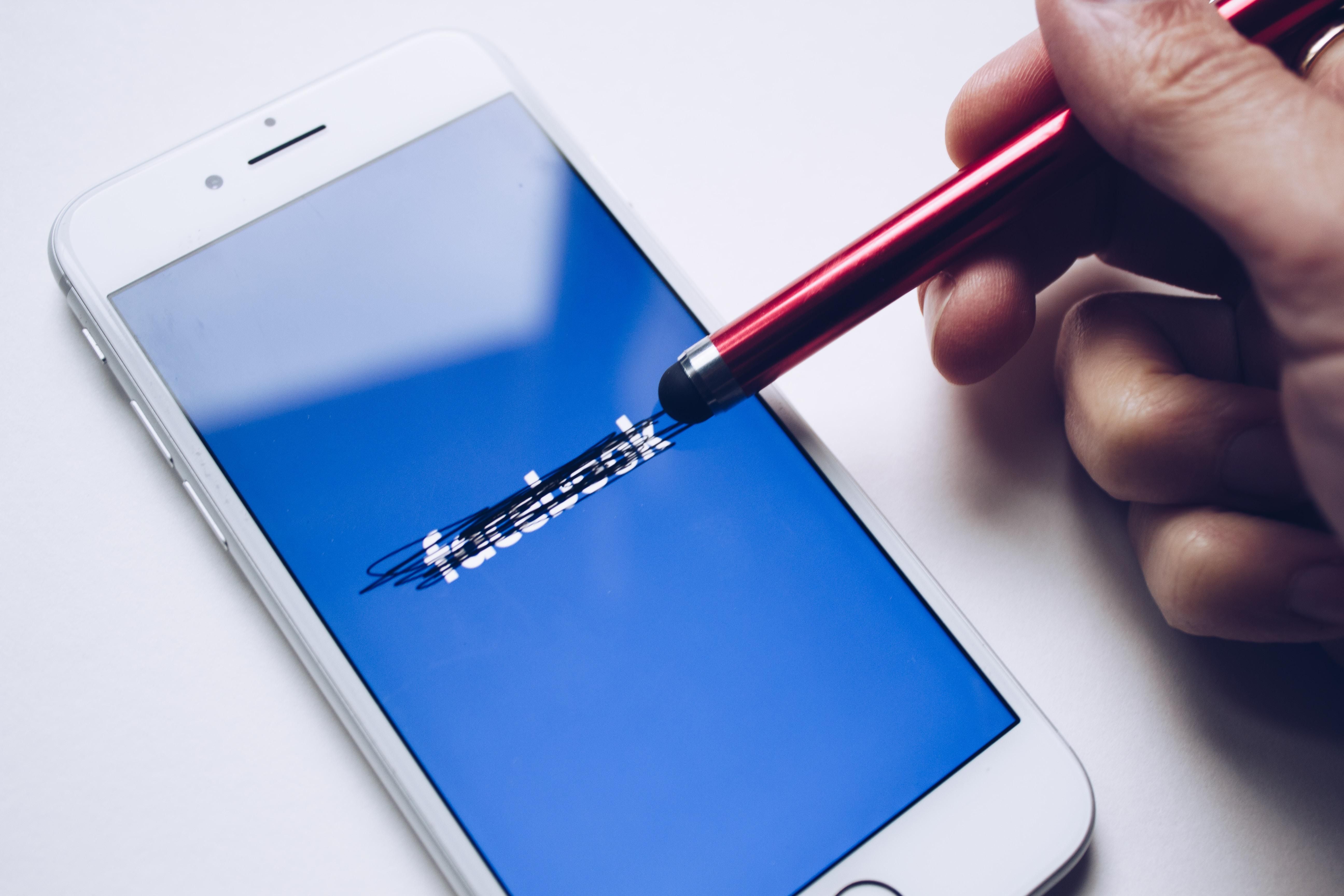 Áthúzott Facebook logó egy okostelefonon és egy toll egy ember kezében