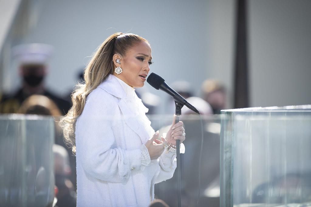 Jennifer Lopez fehér ruhában énekel a színpadon egy mikrofonba